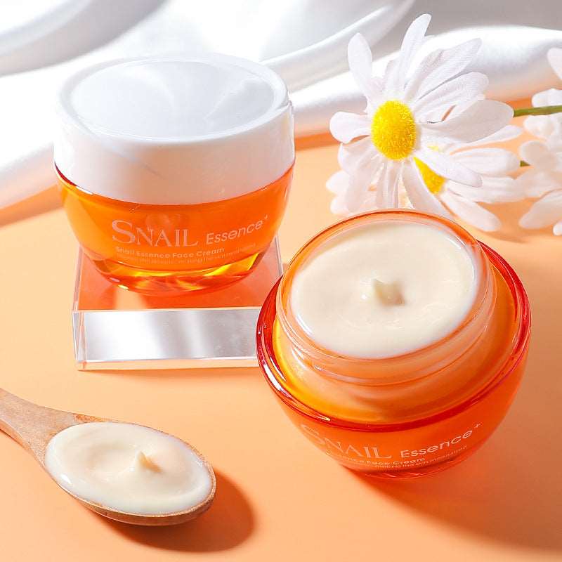 Two jars of Sweet Deals Snail Essence Cream on a peach-colored surface with a white daisy; one jar is open with visible cream and a wooden spoon holding a sample.