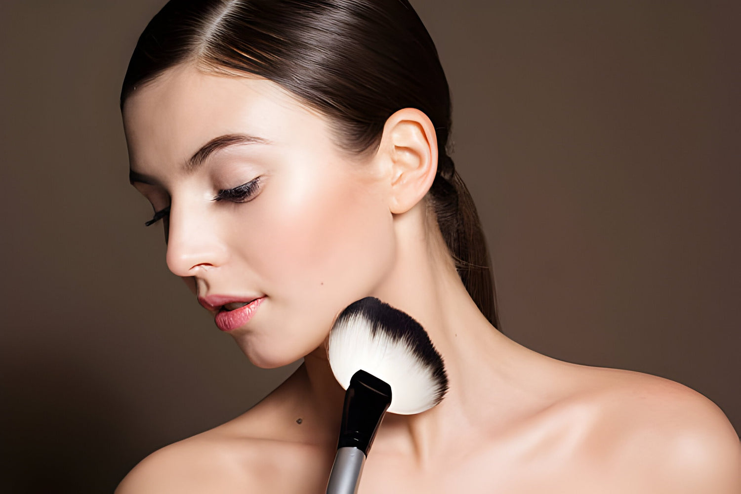 a brunette woman using a make up brush on her face looking to the side darker background