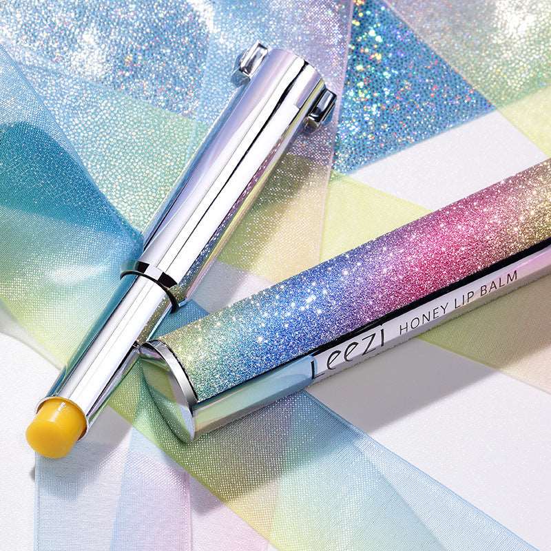 A vibrant image featuring a Rainbow Star Color Changing Lipstick Warm Gradient Lipstick Honey Moisturizing Makeup tube with a yellow cap, resting on a shimmering multicolored pastel background. Brand Name: Sweet Deals